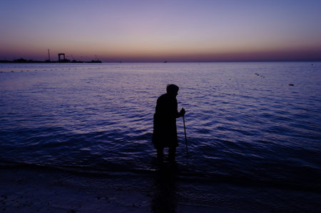 Grandmother with walking sticks walks on the water on The black sea at sunset. This image can use...