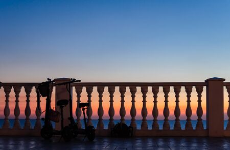Two tourist scooters with a backpack and a women's bag tourists left near the fence with balusters against the sunset by the sea.の写真素材