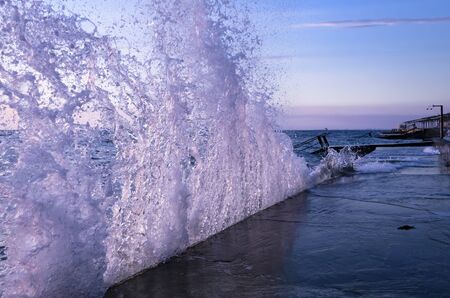Bright sunset under the sea with waves splashes and stones.の写真素材