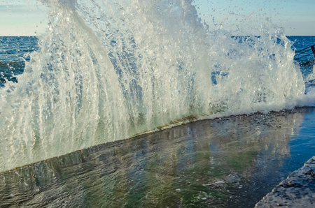 Bright sunset under the sea with waves splashes and stones.の写真素材