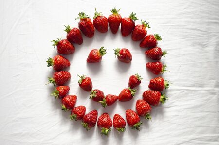 Ripe strawberry berries are laid out on a white background in the shape of a smiley faceの写真素材