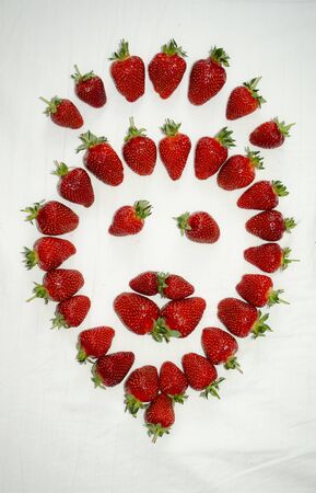 Ripe strawberry berries are laid out on a white background in the shape of a smiley faceの写真素材