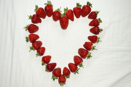 Ripe strawberries are laid out on a white background in the shape of a heartの写真素材