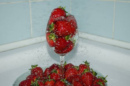 Ripe strawberries in a glass under a stream of water. Red sweet fresh fruit splashing into waterの写真素材