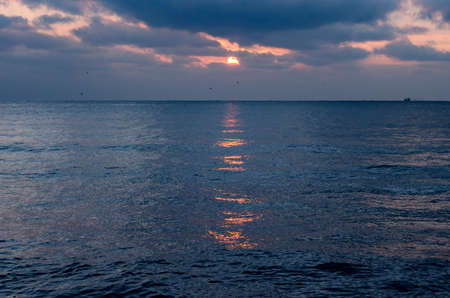 The red sun was half hidden behind the clouds at sunset and a sunny path formed on the sea surfaceの写真素材