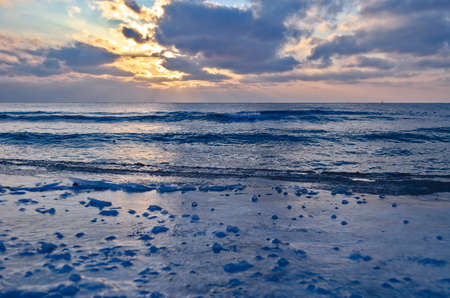 The frozen shore is covered with ice on the background of the sunset by the sea. Cold natural backgroundの写真素材