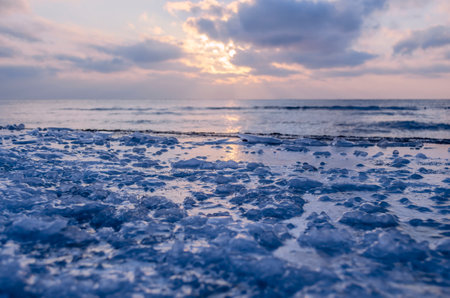 The frozen shore is covered with ice on the background of the sunset by the sea. Cold natural backgroundの写真素材