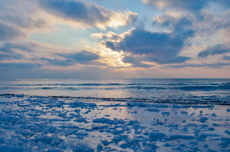 The frozen shore is covered with ice on the background of the sunset by the sea. Cold natural backgroundの写真素材