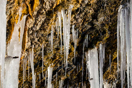 A huge icicle hanging from a rock with moss, which melts and drips into the waterの写真素材