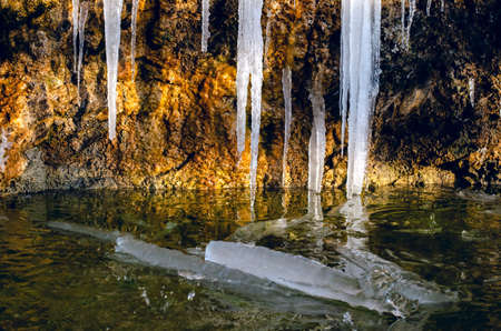 A huge icicle hanging from a rock with moss, which melts and drips into the waterの写真素材