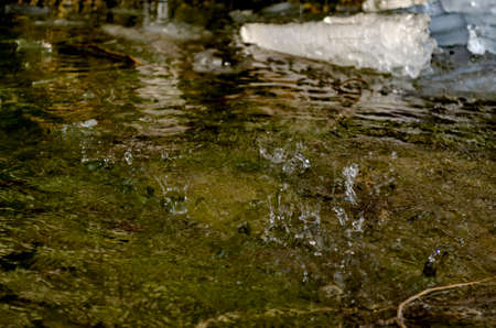 Drops from icicles from the rock drop into the water and form splashes on the waterの写真素材