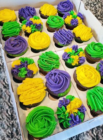Two dozen colorful, purple, lime green and golden yellow Mardi Gras, chocolate, cupcakes in a bakery box.の写真素材