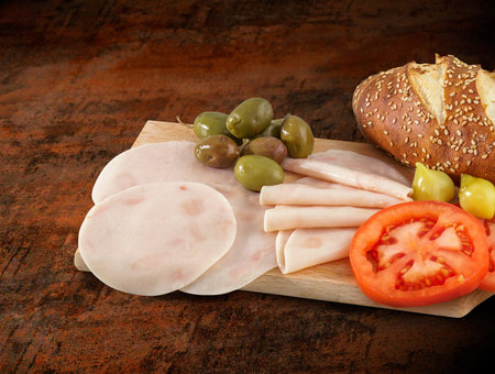 Sliced ham salami decorated on wooden board with olives, tomato and lettuceの写真素材