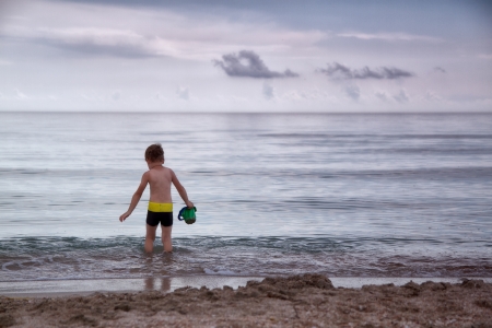 boy walks into cold sea water in a bucket to scoop upの写真素材
