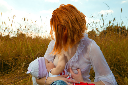 Mother breastfeeding her baby on a great sunny day in a meadow with lots of green grass の写真素材