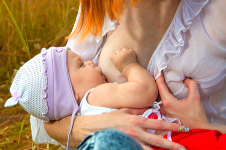 Mother breastfeeding her baby on a great sunny day in a meadow with lots of green grass の写真素材