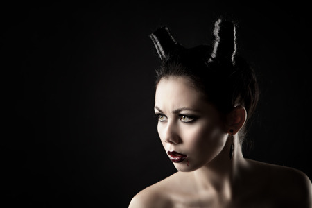The girl in the image of the demon-tempter and hair in the form of horns. Photo taken in the studio on a background.の写真素材