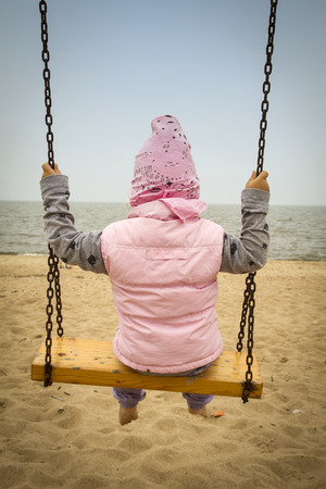 girl sitting on a swing near the sea autumnの写真素材