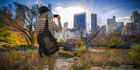 Male tourist takes pictures on a phone in Manhattan Central Parkの写真素材