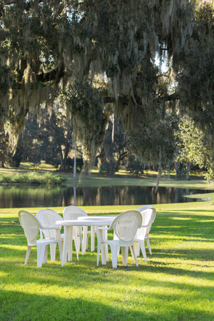 White plastic table and chairs outside in a garden on green lawn by a pond or lake in the afternoon sun and a peaceful relaxing serene tranquil settingの写真素材