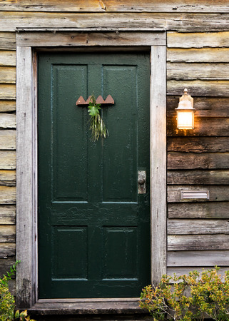 Old rustic vintage dilapidated antique house home building structure with green intricate front door and window with shutters closed and porch light lantern glowing turned onの写真素材