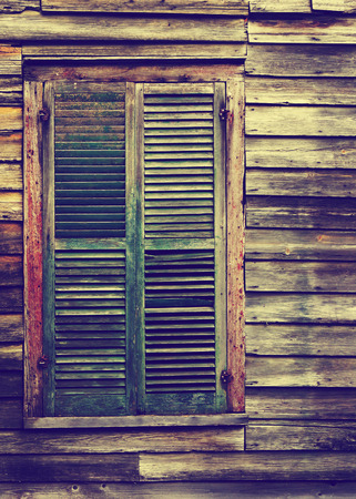 Old rustic vintage antique house home building structure with green intricate front door and window with shutters closed and porch light onの写真素材