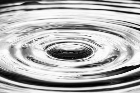 Single solitary drip drop splash of water into reflective colorful calm puddle poolの写真素材