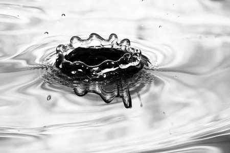 Single solitary drip drop splash of water into reflective colorful calm puddle poolの写真素材