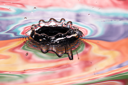 Single solitary drip drop splash of water into reflective colorful calm puddle poolの写真素材