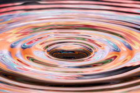 Single solitary drip drop splash of water into reflective colorful calm puddle poolの写真素材