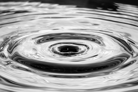 Single solitary drip drop splash of water into reflective colorful calm puddle poolの写真素材