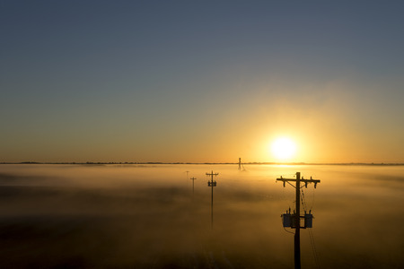 Telephone poles on a foggy misty morning at sunrise or sunset on a rural countryside farmの写真素材