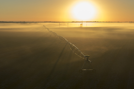 Rural farm countryside pivot irrigation system on an empty barren field at sunrise or sunset in the fog or mistの写真素材