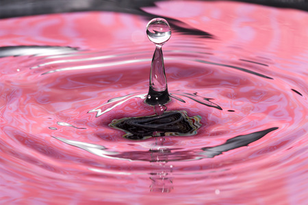 Single solitary drip drop splash of water into reflective colorful calm puddle poolの写真素材