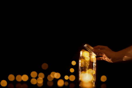 Clear transparent jar jug glass container with magical balls dots bits of bokeh light leaving escaping or being released let go free from confinement capture isolated on black backgroundの写真素材