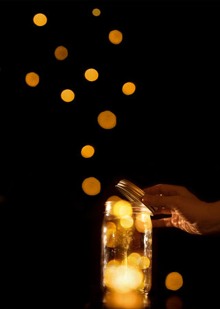 Clear transparent jar jug glass container with magical balls dots bits of bokeh light leaving escaping or being released let go free from confinement capture isolated on black backgroundの写真素材