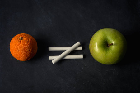 Orange does not equal apple with chalk on top of chalkboard suggesting inequality in different fruitの写真素材