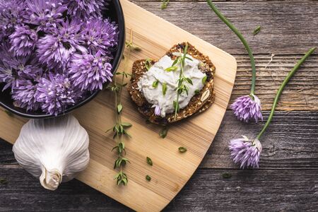 A delicious garlic and chive cream cheese spread on herbed crackers next to a bowl of purple chive flowers.の写真素材