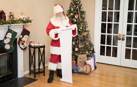 Santa reading his naughty or nice list in a living room decorated for Christmas.のeditorial素材