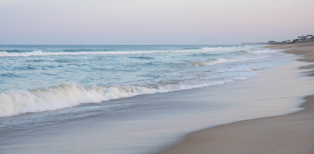 Waves crashing ashore at dusk with a pier off in the distance.