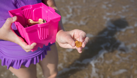A close up photo of a girl holding a bucket and a heart shaped rock she found while collecting seashells at the beach.の写真素材