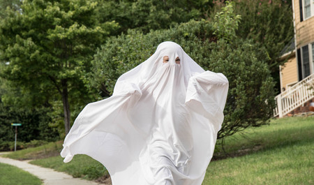 A child in a ghost costume made out of a bedsheet running down the sidewalk.