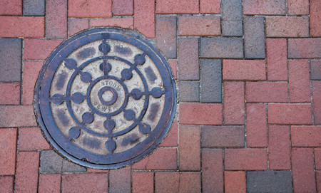 Close up photo of a storm sewer manhole cover on a brick sidewalk.の写真素材
