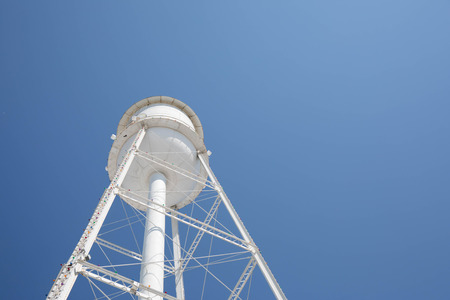 Looking up at a bright white water tower from below with a bright blue cloudless sky.の写真素材