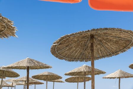 Wicker and textile orange umbrellas on the beach. Blue sky.の写真素材