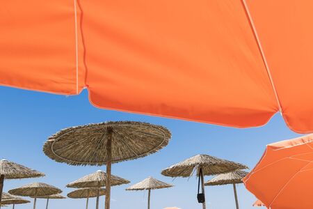 Wicker and textile orange umbrellas on the beach. Blue sky.の写真素材