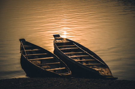 Wooden fishing boat standing in the riverbank in autumn sunset. Sunset reflection on the water, peaceful landscapeの写真素材