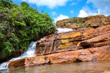 The landscape of a small waterfall beside a forest with beautiful blue cloudy sky. Water brooking from the small mount to the river bed in monsoonの写真素材