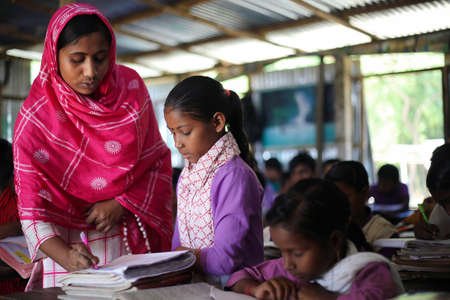Gowainghat, Bangladesh - November 06, 2019: Community teacher in the class busy checking the notebook, math homework by students. The teacher is finding mistake and teaching the student how to do it.のeditorial素材