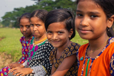 Gowainghat, Bangladesh â November 06, 2019: Selective focus on the girls staring at the camera and smiling. Little poor girl smiling sitting on the grass with other friends along with her.のeditorial素材